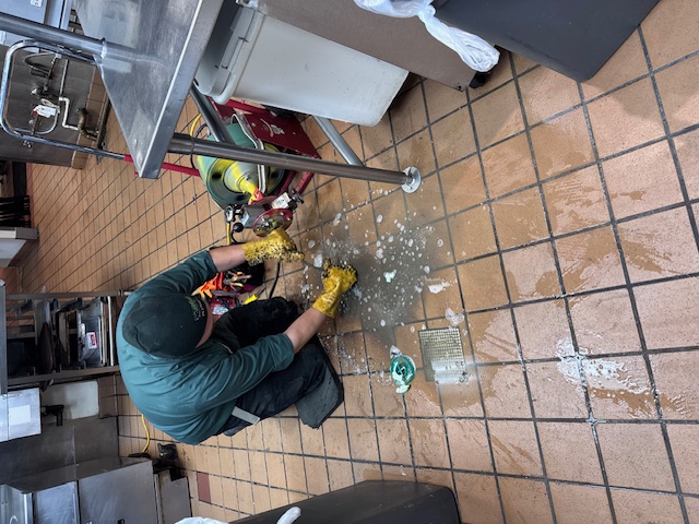 Drain Cleaning Services in Kent -Rush Plumbing main in restaurant kitchen cleaning out drain with equipment