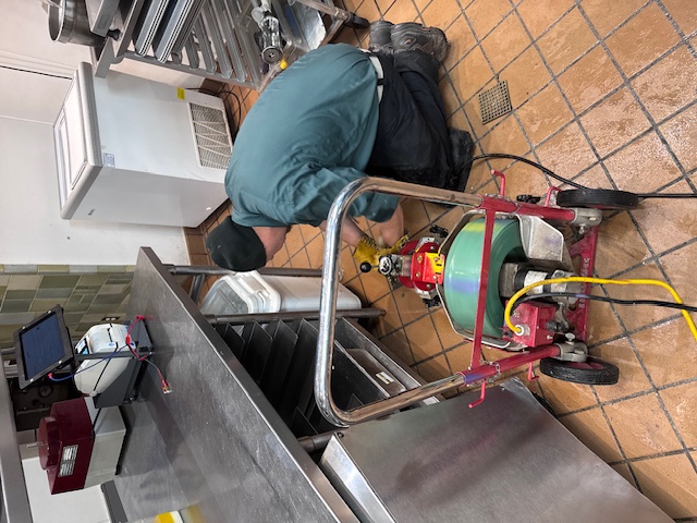 Drain Cleaning Services in Kent -Rush Plumbing main in restaurant kitchen cleaning out drain with equipment